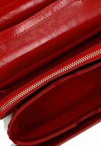 Rote Lederhandtasche mit einer glatten Textur, ausgestattet mit einem goldenen Reißverschluss. Das Innenfutter ist ebenfalls rot und bietet ein geräumiges Hauptfach.