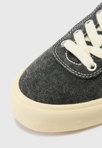 Sneaker in tela grigio scuro con lacci bianchi, caratterizzato da una punta rotonda e una suola in gomma cremosa texturizzata. I fori per i lacci sono in metallo e rinforzati.
