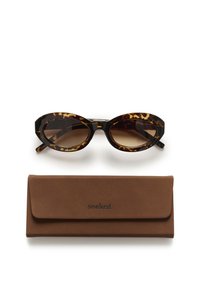 Zonnebril met tortoise-achtig montuur en verloopbruin glazen, vergezeld van een bruine leren hoes met het label "soaked."