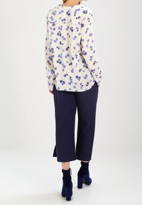 Blouse florale en crème et bleu, en tissu léger. Assortie à un pantalon large marine et des bottines bleues. Vue de dos, coupe décontractée.