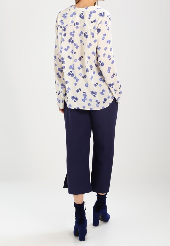 Blouse florale en crème et bleu, en tissu léger. Assortie à un pantalon large marine et des bottines bleues. Vue de dos, coupe décontractée.