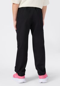 Pantalones cargo negros con una cintura elástica y bolsillos laterales, combinados con zapatillas deportivas rosas con textura de malla y suelas blancas.