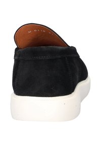 Zwarte suede instapper met een witte rubberen zool en een bruine leren voering zichtbaar bij de hiel. Minimale stikseldetails bij de naden.