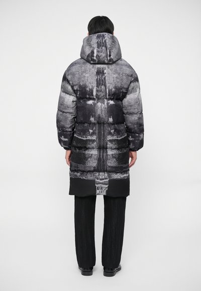 Abrigo tipo puffer en tonos de gris con un estampado texturizado, con capucha y diseño largo. Combinado con pantalones y zapatos negros.