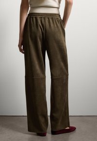 Olivgrüne weit geschnittene Hose aus weichem Velours, mit elastischem Bund und dezenten Nähten. Knöchellang mit minimaler Gestaltung.