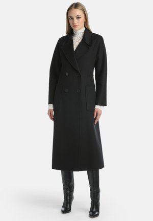 Musta kaksirivinen takki, jossa on läpällinen kaulus, sivutaskut ja pitkät hihat; valmistettu paksusta, tekstuurista kankaasta.