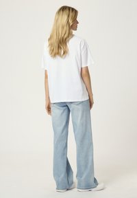 T-shirt blanc à manches courtes avec une coupe décontractée, associé à un jean large bleu clair et des baskets blanches. La vue arrière montre un design et une coupe simples.