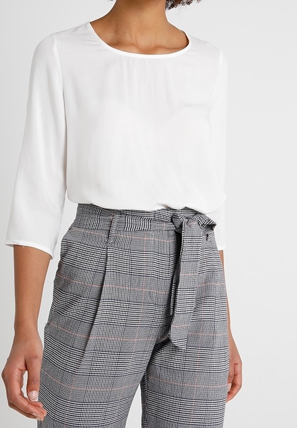 Vit blus med trekvartsärmar som är ihopparad med högmidjade grå rutiga byxor som har ett tygbälte knutet i en rosett.