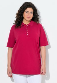 Polo a maniche corte in fucsia con patta di bottoni e colletto; realizzato in cotone; texture liscia; vestibilità comoda, indossato con pantaloni bianchi.