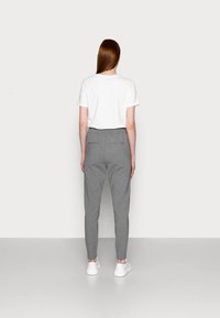 Grå tapered bukser med elastisk talje, der har to baglommer, parret med en ensfarvet hvid t-shirt og hvide sneakers.