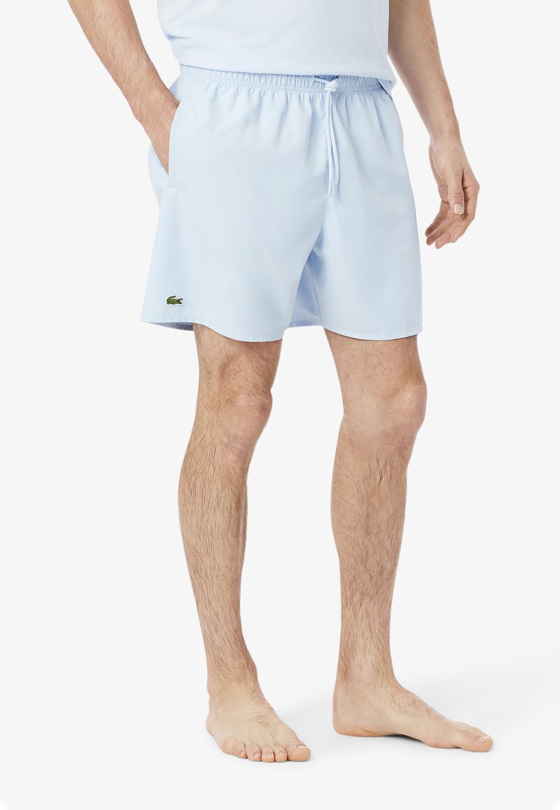 Lichtblauwe zwemshorts gemaakt van een zachte stof; heeft een elastische tailleband met een trekkoord, zijzakken, en een groen logo op de zoom.