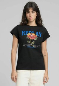 Maglietta nera con maniche corte arrotolate, con grafica colorata di una rosa e scritta "REPLAY" in blu. Realizzata in tessuto morbido, vestibilità casual.