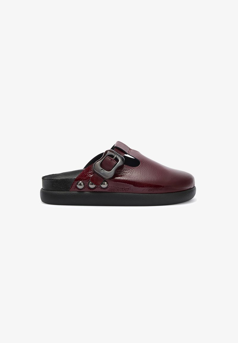 Sandalia deslizante de cuero burdeos con punta redonda, un detalle de hebilla y tachuelas plateadas en el lateral. Suela de goma negra y acabado texturizado.
