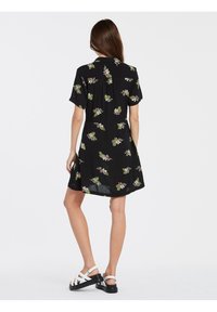 Vestido negro de manga corta con estampado floral en verde y rosa. Cuello simple y corte relajado, con un dobladillo ligeramente acampanado.