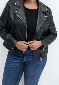 Chaqueta de moto de cuero negra con cremalleras plateadas, cierres a presión y un diseño corto. Llevada sobre una camiseta negra y jeans de denim azul.