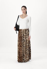 Top bianco a maniche lunghe con scollatura a V profonda, abbinato a una lunga gonna con stampa leopardata. Il modello tiene una borsa nera in un tessuto strutturato.