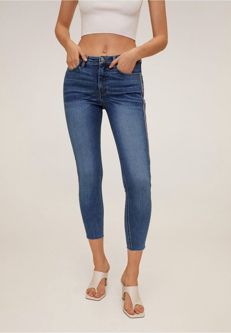 Jeans ajustados de denim azul oscuro con una cintura alta y un largo cropped. Presenta costuras laterales sutiles y un ligero deshilachado en el dobladillo.