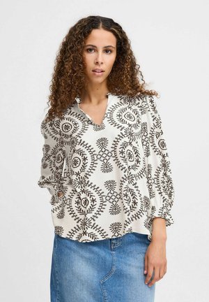Hvid mønstret bluse med sorte blomsterdesigns, med en V-udskæring, lange puffærmer og en afslappet pasform. Sammen med en denimnederdel.