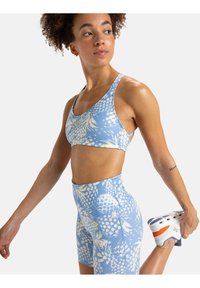 Un reggiseno sportivo azzurro chiaro e pantaloni corti a vita alta abbinati con motivi floreali, realizzati in un materiale morbido ed elastico. Sneakers bianche con dettagli arancioni.