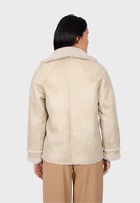 Giacca in suede beige con colletto e polsini in pelliccia crema, caratterizzata da una vestibilità dritta e dettagli di cucitura visibili. Texture morbida e design accogliente.