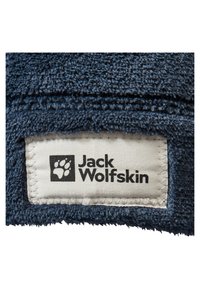 Dunkelblauer, strukturierter Stoff mit einem gewebten Etikett, das "Jack Wolfskin" und ein Pfotenlogo zeigt, auf einer Kante mit beigem Garn genäht.