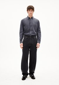 Donkerdenim overhemd met knopenkraag, borstzak, gecombineerd met wijde zwarte jeans en zwarte leren schoenen. Vlakke textuur, casual ontwerp.