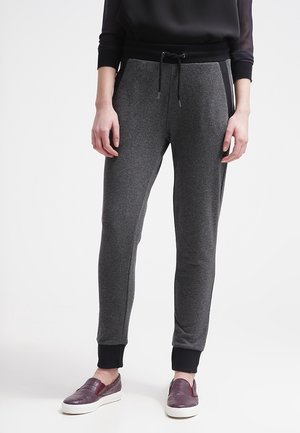 Osoba ubrana w ciemnoszare spodnie dresowe z czarnymi mankietami i sznurkiem, połączone z bordowymi butami wsuwanymi i czarną bluzką z długim rękawem.