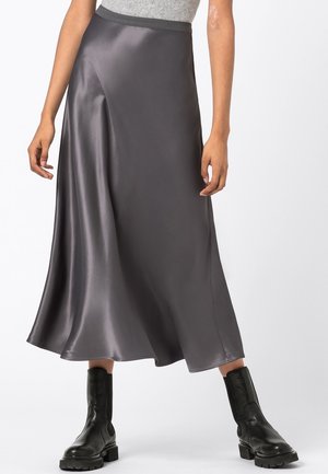 Een grijze satijnen midirok met een gladde textuur en vloeiend ontwerp, voorzien van een elastische tailleband voor comfort. Gecombineerd met zwarte enkellaarsjes.