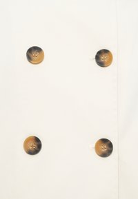 Quatre boutons ronds marron et noir disposés en deux rangées verticales sur un fond en tissu blanc.
