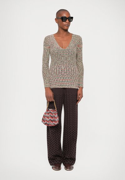 Pull en tricot multicolore avec un col en V, manches longues, associé à un pantalon à motif zigzag sombre. Les accessoires comprennent un petit sac à motifs.