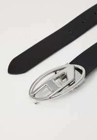 Black leather belt featuring a silver metal buckle with an oval shape and a central cut-out detail. Smooth texture throughout the band.