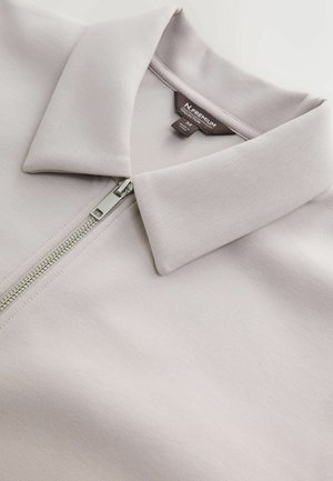 Světle levandulová zipová bunda s plochým límcem, hladkým materiálem a lesklým stříbrným zipem. Viditelné štítky uvnitř.