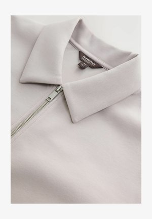 Ljust lavendelfärgad zip-jacka med platt krage, slät tyg och glänsande silverdragkedjedetalj. Taggar synliga på insidan.