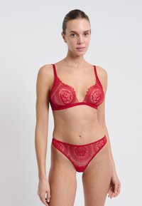 Soutien-gorge en dentelle rouge et string assorti avec un motif floral, une texture transparente et des bretelles fines. Les deux pièces présentent des bordures décoratives et un design sculptant.
