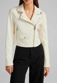 Biała krótka kurtka z sztucznej skóry z klapowym kołnierzem, zamkiem błyskawicznym z przodu i dwoma kieszeniami na zamek. Gładka tekstura z srebrnymi elementami ozdobnymi.