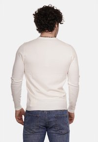 Maglione a maniche lunghe color crema con un design aderente, polsini a coste e una texture liscia, abbinato a jeans in denim blu.