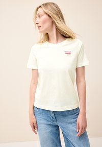 T-shirt en coton jaune clair à manches courtes, décolleté rond et logo "amore verde" brodé en rose sur la poitrine. Design à coupe décontractée.