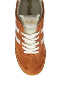 Scarpa sportiva in suede marrone con strisce e lacci bianchi, dotata di una linguetta beige con la scritta "Gola" in caratteri dorati e suola in gomma.