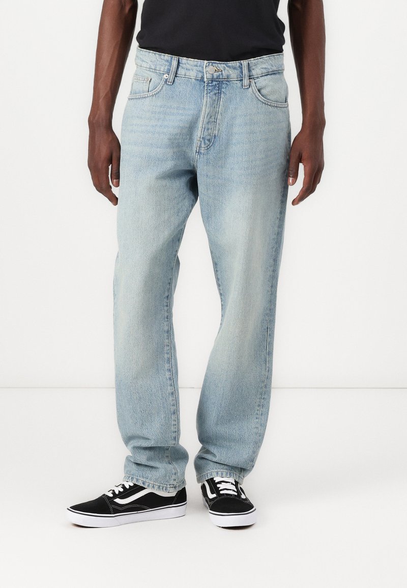 Lichtblauwe denim jeans met een rechte snit, voorzien van riemlussen, zakken en een vervaagde textuur. Gecombineerd met zwarte Vans-schoenen.