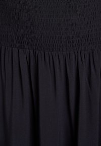 Robe noire avec un buste smocké et une jupe plissée. Le tissu semble doux avec un léger éclat. Elle présente un haut texturé et élastique.