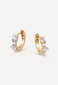 Boucles d'oreilles en or en forme de créole, ornées de trois pierres claires étincelantes montées en sertissage griffes, avec une surface lisse et polie et un design courbé.