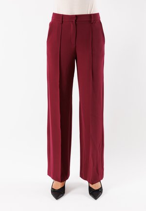 Pantaloni a gamba larga bordeaux in tessuto morbido con pieghe frontali, vita piatta e tasche laterali, abbinati a scarpe nere con punta affilata.
