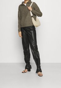 Pull tricot vert olive avec un col demi-fermeture éclair, assorti à un pantalon en cuir noir taille haute avec des poignets noués et des talons ouverts noirs.