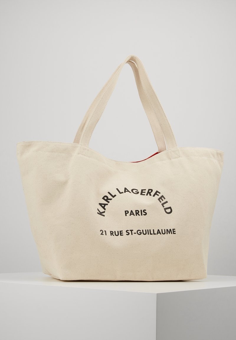 Beige canvas tote bag with dual handles, featuring black text "KARL LAGERFELD PARIS 21 RUE ST-GUILLAUME" on front.
