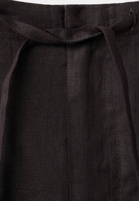 Gros plan d'un pantalon en tissu noir avec un cordon de taille noué et des détails de couture visibles.