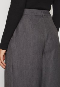 Grijze wijde broek met een gladde textuur, voorzien van voorplooien en een op maat gemaakte tailleband. Geen zichtbare zakken of hardware details.