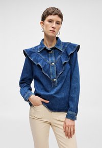 Τζιν πουκάμισο με μεγάλο φουσκωτό γιακά, κουμπιά μπροστά με χρυσά κουμπιά και μακριά μανίκια. Χρώμα: μπλε. Απαλή υφή.