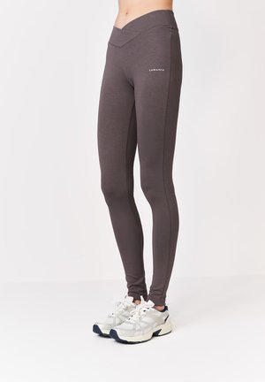 Zbliżenie osoby noszącej dopasowane, ciemnoszare legginsy z pasem w kształcie litery V oraz białe sportowe buty.