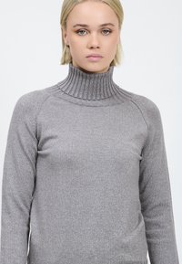 Maglione grigio a coste con collo alto e maniche lunghe. Realizzato in un materiale leggermente lucido. Presenta una vestibilità aderente e un colletto alto.
