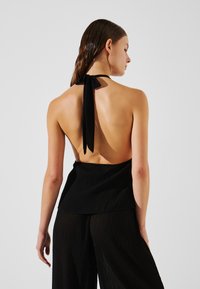 Juoda viršutinė dalis su sagtimi nugaros dalyje, pasižyminti tekstūruotu audiniu ir atvira nugara, derinama su juodomis plačiomis kelnėmis.